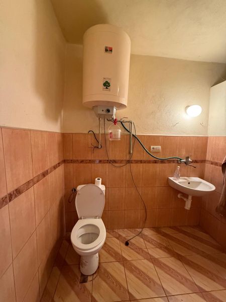 Badezimmer mit Toilette, Wassererhitzer, Waschbecken, Boden mit Holzdekor in einem Einfamilienhaus.