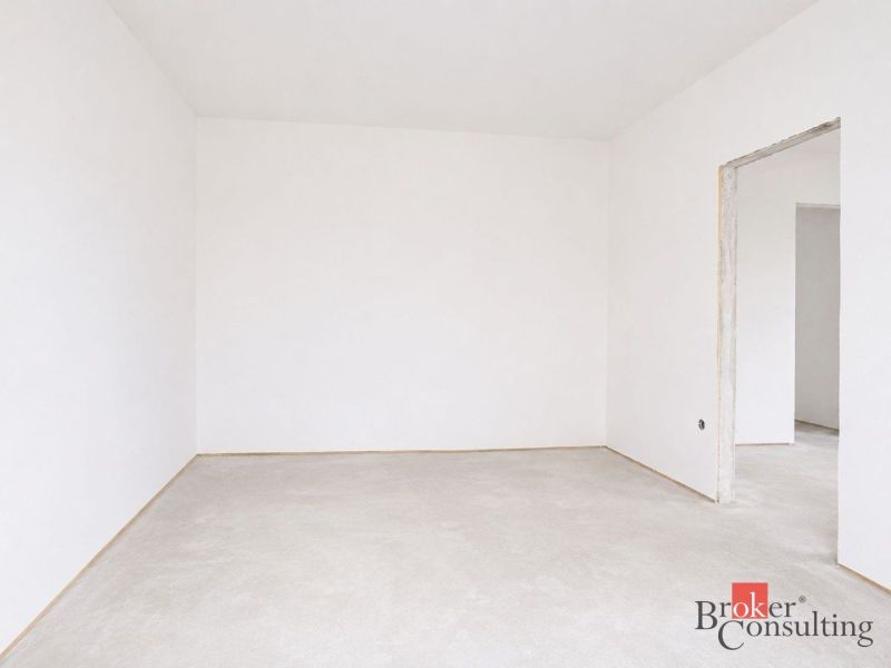 Leerer Raum in einer 4-Zimmer-Wohnung mit weißen Wänden und Betonboden.