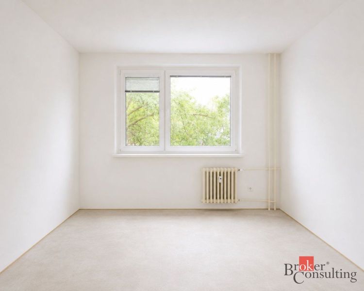 Ein helles Zimmer mit Bäumen vor dem Fenster, einem Heizkörper und einem Boden mit Holzdekor in einer 4-Zimmer-Wohnung.