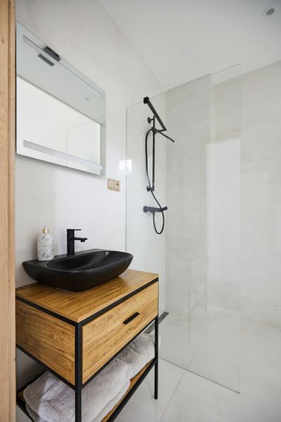 Badezimmer in einer 3-Zimmer-Wohnung mit schwarzem Waschbecken, Dusche und Holzelementen.