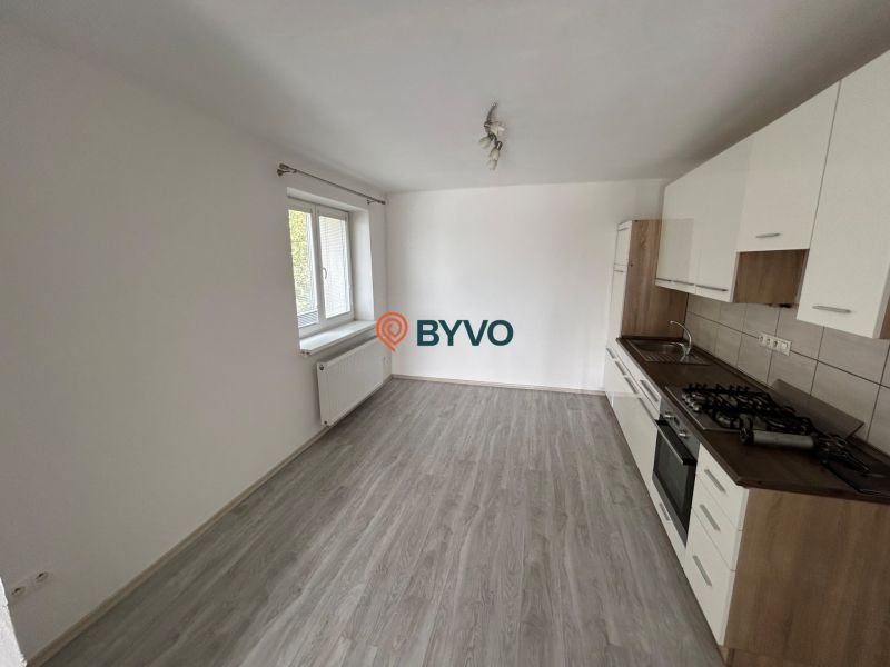 Küche mit weißer Küchenzeile in einer 3-Zimmer-Wohnung, Boden mit Holzdekor, großes Fenster.