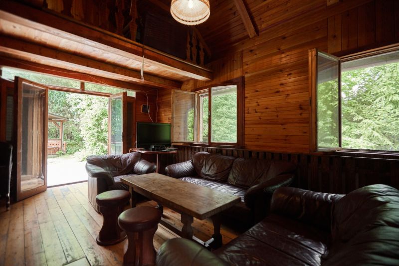 Eine Hütte mit einem Boden in Holzoptik, einem Ledersofa und großen Fenstern mit Aussicht.