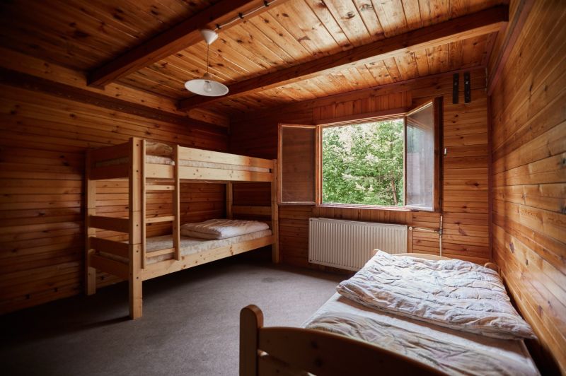 Ein Schlafzimmer in einer Hütte mit einem Etagenbett, Holzverkleidung und offenem Fenster.