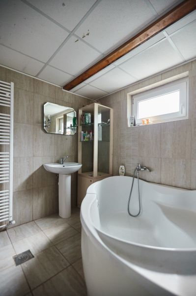 Badezimmer in der Hütte mit Badewanne, Waschbecken, Spiegel und Regalen für Toilettenartikel.