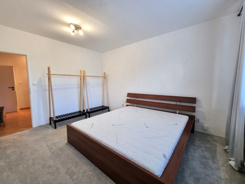 Schlafzimmer mit Bett und Kleiderständer in einer 2-Zimmer-Wohnung, Boden mit Holzdekor.
