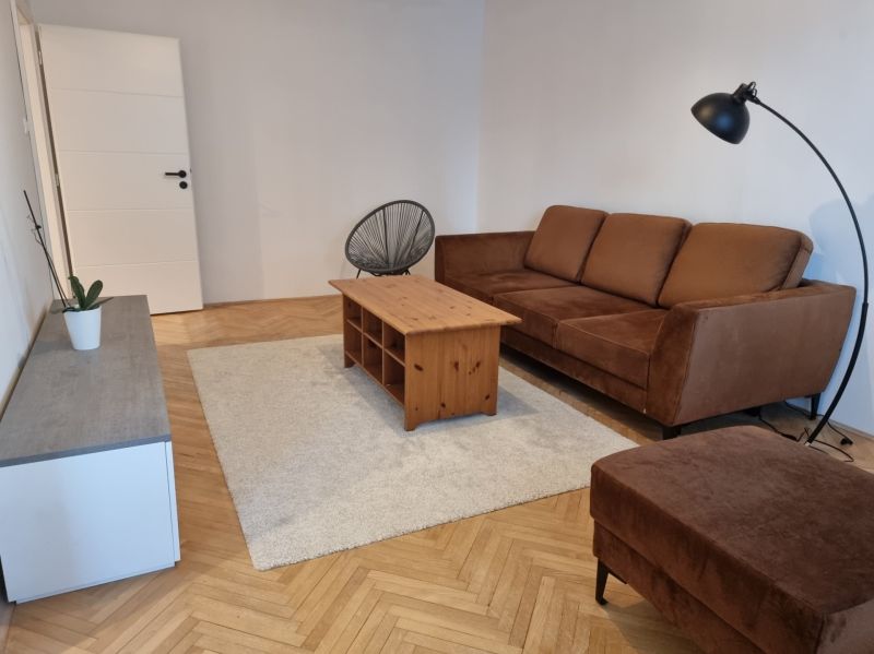 Wohnzimmer in einer Zweizimmerwohnung, braunes Sofa, Couchtisch, Boden mit Holzdekor.
