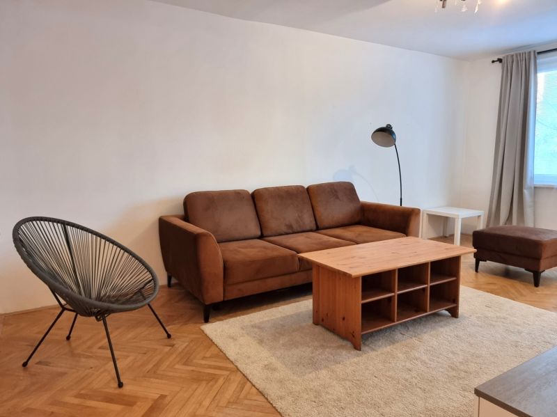 Wohnzimmer einer Zweizimmerwohnung mit braunem Sofa und Boden in Holzoptik.