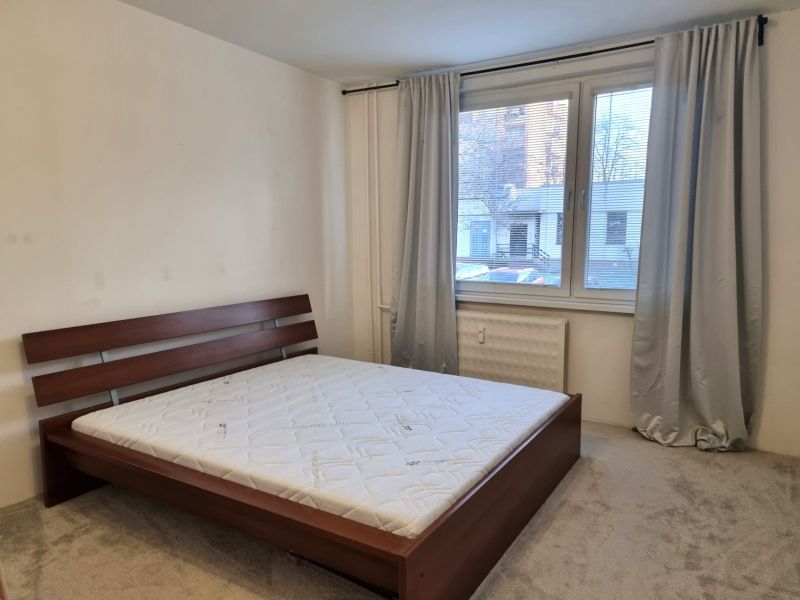 Schlafzimmer mit grauen Vorhängen, großem Fenster und Bett in einer 2-Zimmer-Wohnung.