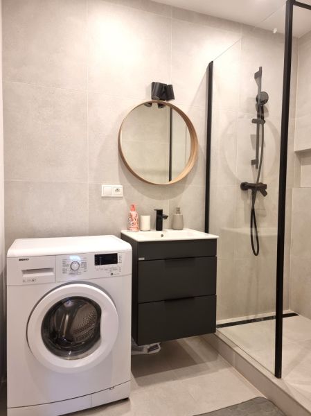 Badezimmer mit Waschmaschine, Duschkabine und rundem Spiegel in einer 2-Zimmer-Wohnung.
