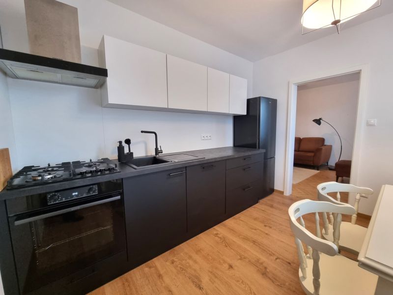 Küche in einer 2-Zimmer-Wohnung mit schwarzen Geräten und einem Boden in Holzoptik.