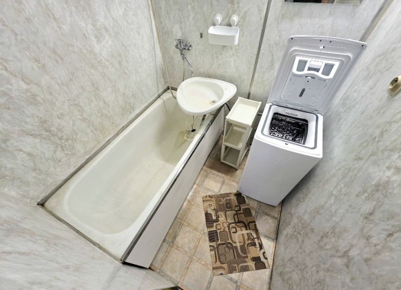 Badezimmer in einer 3-Zimmer-Wohnung mit Badewanne, Waschmaschine und Fliesen.