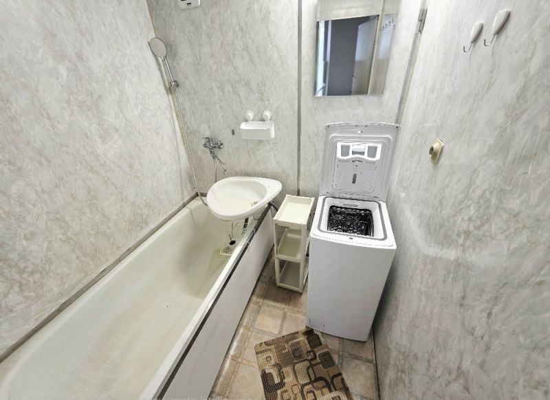 Badezimmer mit Badewanne, Toilette, Waschmaschine und Spiegel in einer 3-Zimmer-Wohnung.