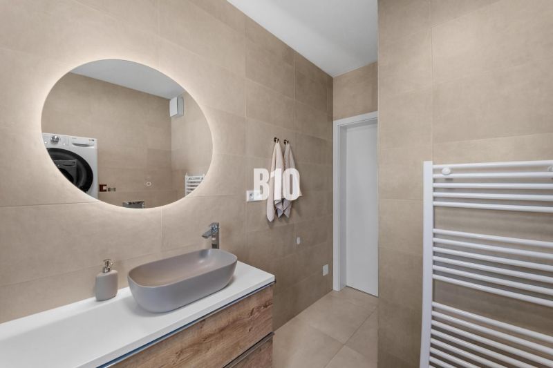 Badezimmer in einer 4-Zimmer-Wohnung mit rundem Spiegel und Waschbecken an beigefarbenen Wänden.