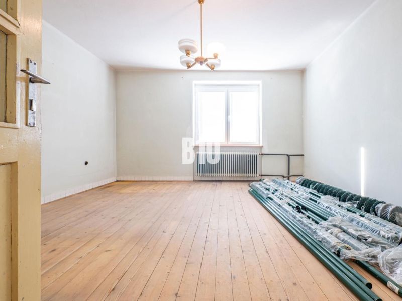 Ein Raum in einem Einfamilienhaus mit einem Holzboden und einem Stapel Stangen am Fenster.