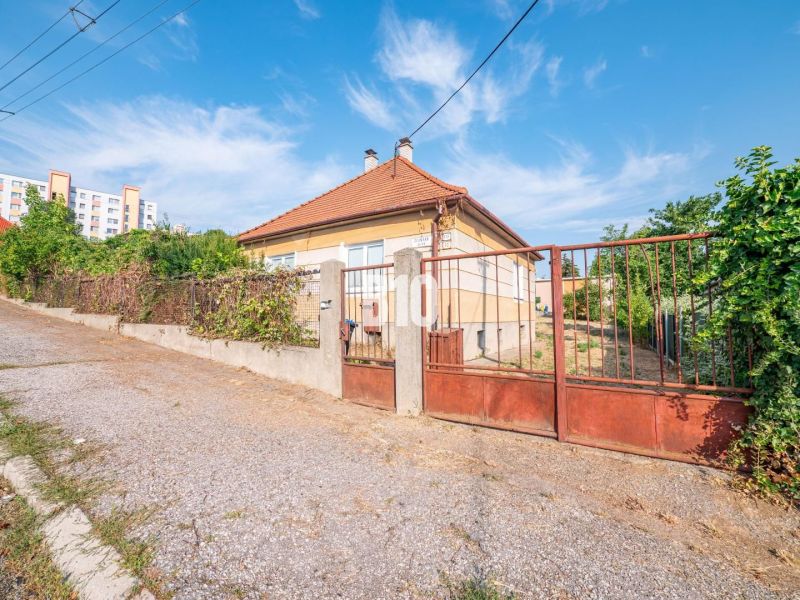 Ein Einfamilienhaus in Nitra mit einem Zaun und einem Schrägdach, im Hintergrund ein Plattenbau.
