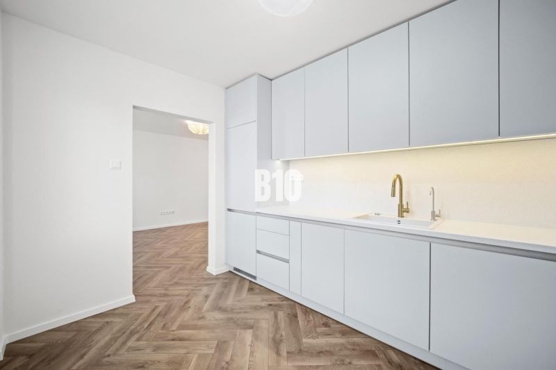 Küche in einer 3-Zimmer-Wohnung mit weißen Möbeln und einem Boden in Holzoptik.