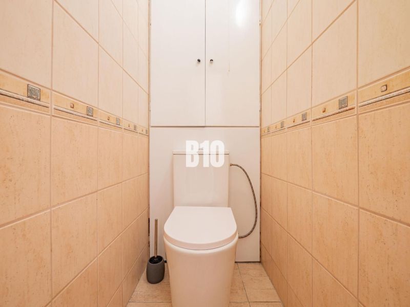 Toilette mit beigefarbenen Fliesen in einer Einzimmerwohnung, praktisches Design und Stauraum.