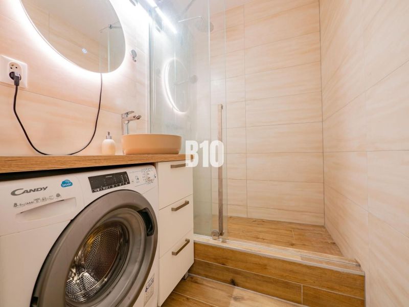 Badezimmer in einer Einzimmerwohnung mit Waschmaschine, Spiegel und Boden in Holzoptik.