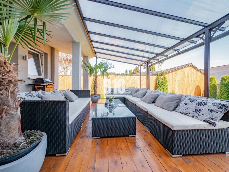 Die Terrasse des Einfamilienhauses in Nitra mit Rattanmöbeln und einem Boden in Holzoptik.