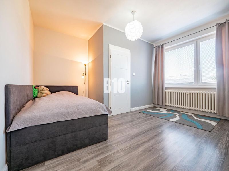 Ein Zimmer in einem Einfamilienhaus mit einem Boden in Holzoptik, einem Bett und einem Teppich.