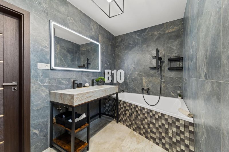 Badezimmer in einem Einfamilienhaus mit Badewanne, Steinverkleidung und großem Spiegel.