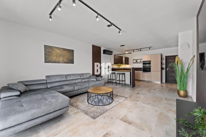 Wohnzimmer in einem Einfamilienhaus mit bequemer Couch, Küche und Boden in Holzoptik.