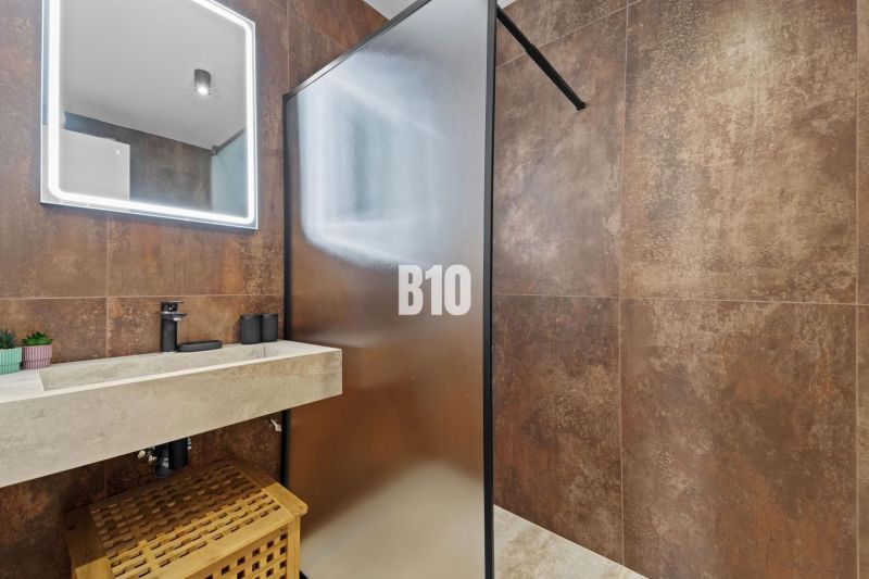 Badezimmer mit durchsichtiger Duschwand, steinernem Waschbecken und dekorativer Beleuchtung.