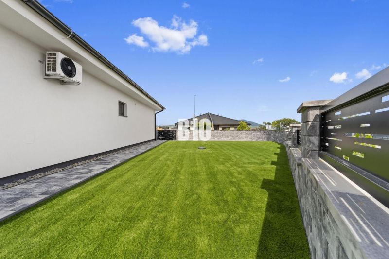Der Garten eines Einfamilienhauses in Nitra mit Rasen und Steinpflaster an der Wand.