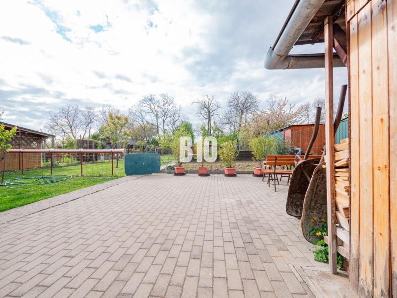 Der Hof eines Einfamilienhauses in Nitra mit einer gepflasterten Terrasse, Grünflächen und einem Holzschuppen.