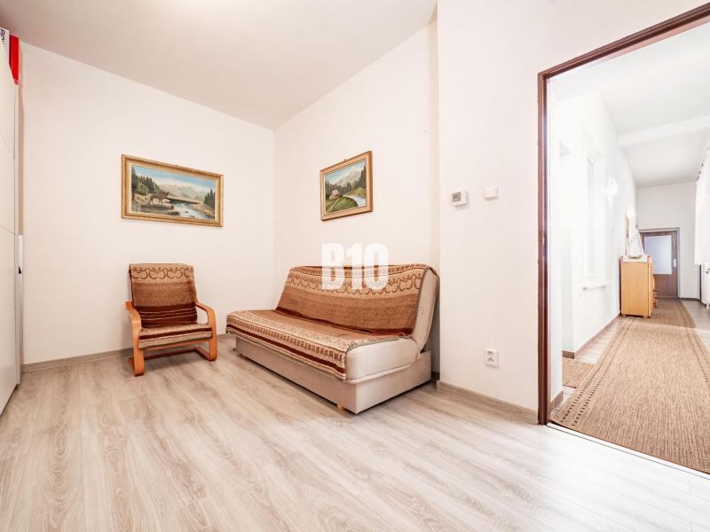 Ein Zimmer in einem Einfamilienhaus mit einem Sofa, einem Sessel und einem Boden in Holzoptik.