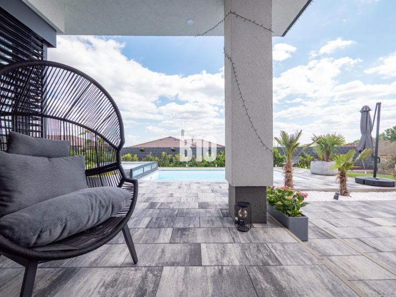 Ein Einfamilienhaus in Nitra mit Terrasse, Pool, Rattansessel und Palmen.