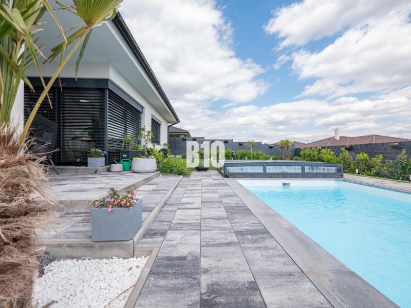 Ein Einfamilienhaus in Nitra mit Terrasse, Pool, Pflastersteinen und exotischen Pflanzen.