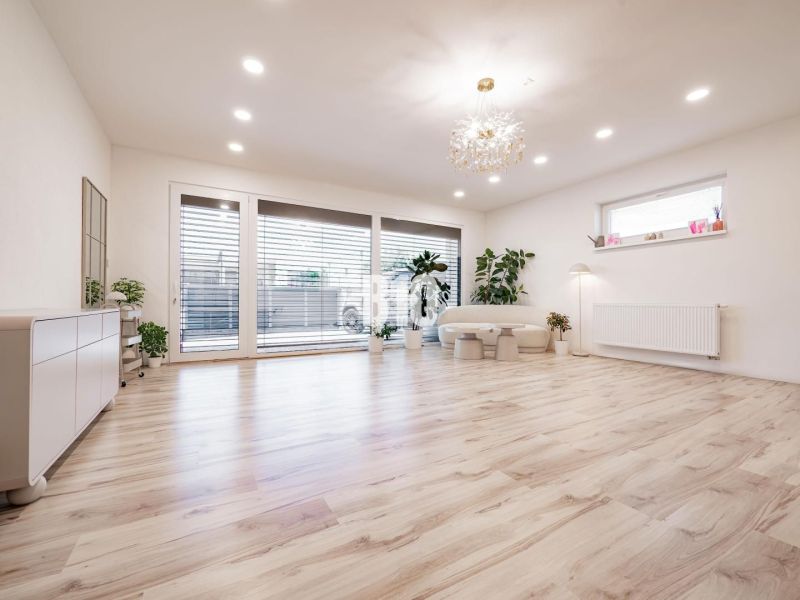 Helles Wohnzimmer mit Holzdekorboden, großen Fenstern und Pflanzen.