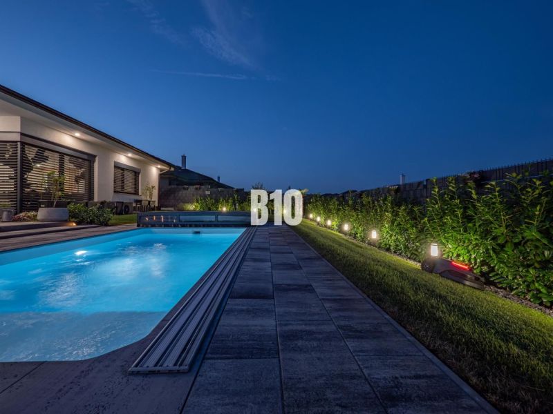 Nachtgarten bei einem Einfamilienhaus in Nitra mit beleuchtetem Pool und Terrasse.