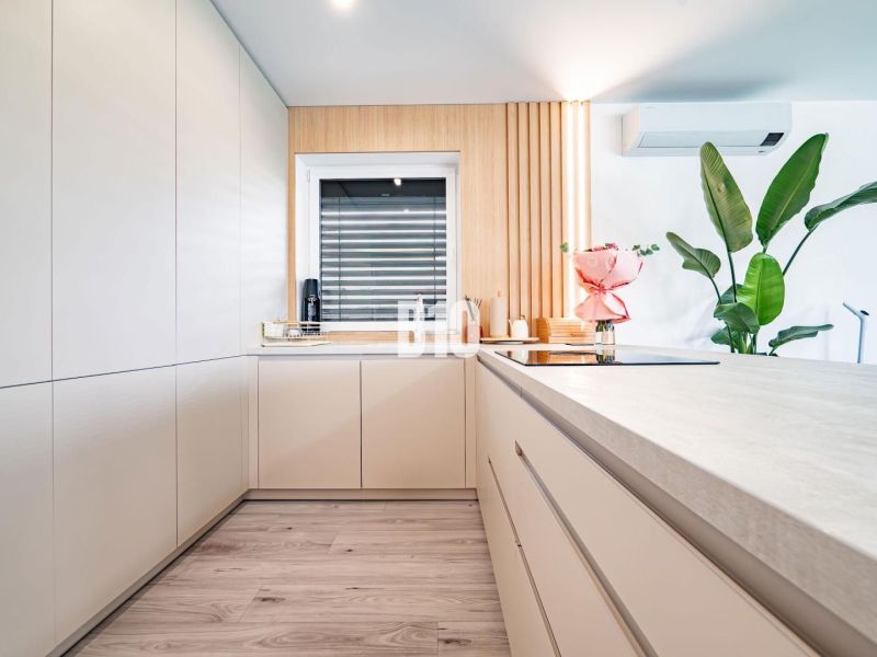 Eine Küche in einem Einfamilienhaus mit Holzboden, weißen Schränken und Blumen.