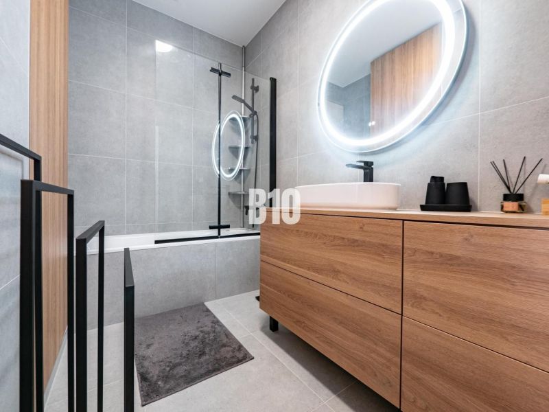 Badezimmer mit Holzdekor in einem Einfamilienhaus, mit Badewanne und ovalem Spiegel mit Beleuchtung.
