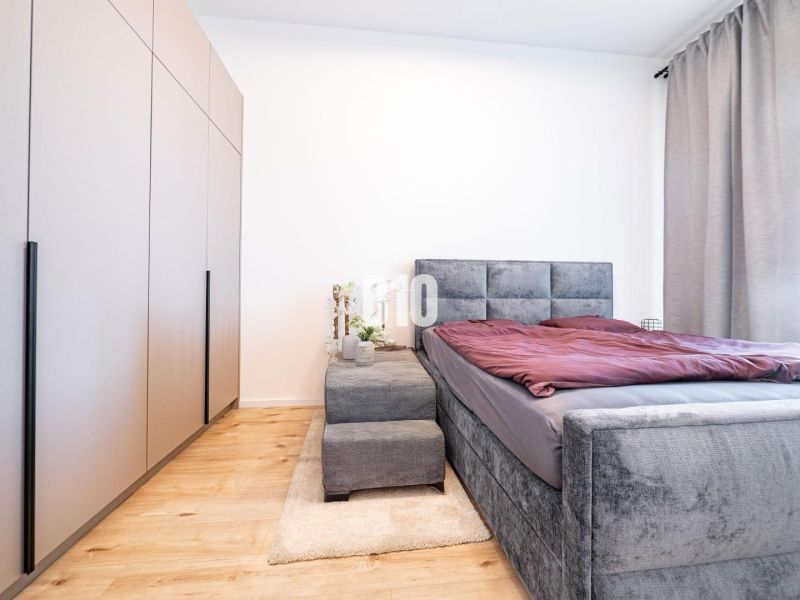 Ein Schlafzimmer in einem Einfamilienhaus mit Bett, Kleiderschrank und einem Boden in Holzoptik.
