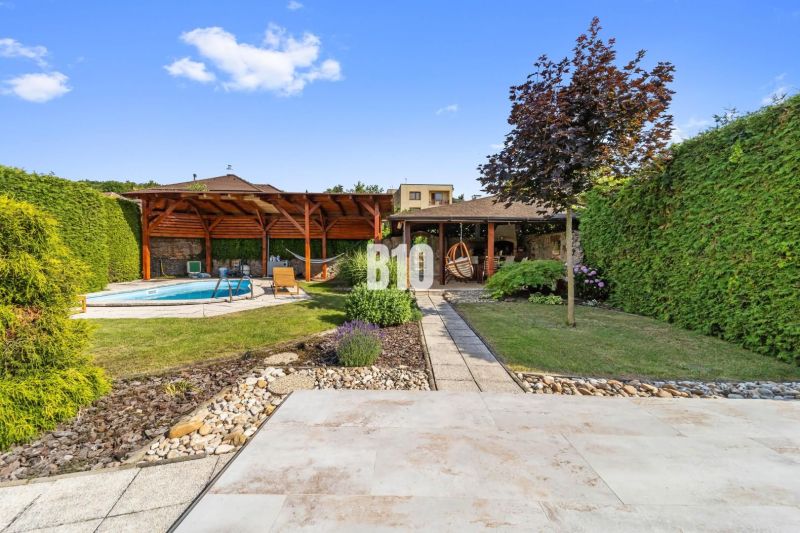 Der Garten eines Einfamilienhauses in Nitra mit einem Pool und einem Pavillon, umgeben von Grün.