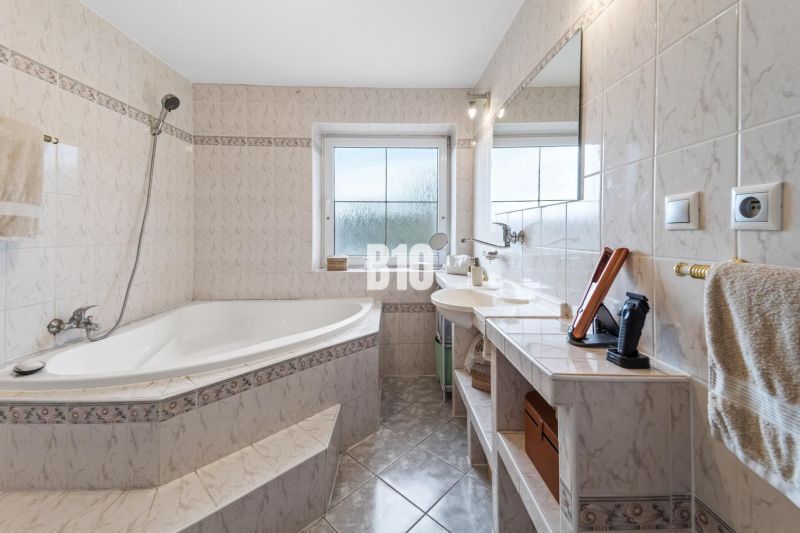 Ein Badezimmer im Einfamilienhaus mit einer Eckbadewanne und einem Fenster, helle Fliesen.