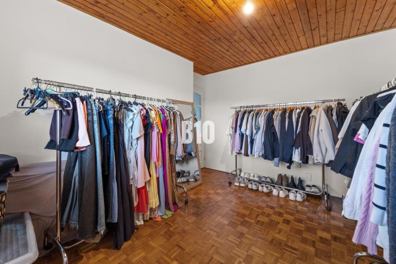 Ein Kleiderschrank im Einfamilienhaus mit Kleiderstangen und einem Boden in Holzoptik.