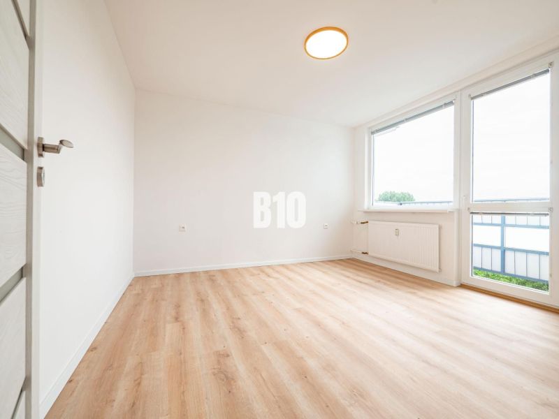 Ein Zimmer in einer 3-Zimmer-Wohnung mit einem Holzboden und großen Fenstern.