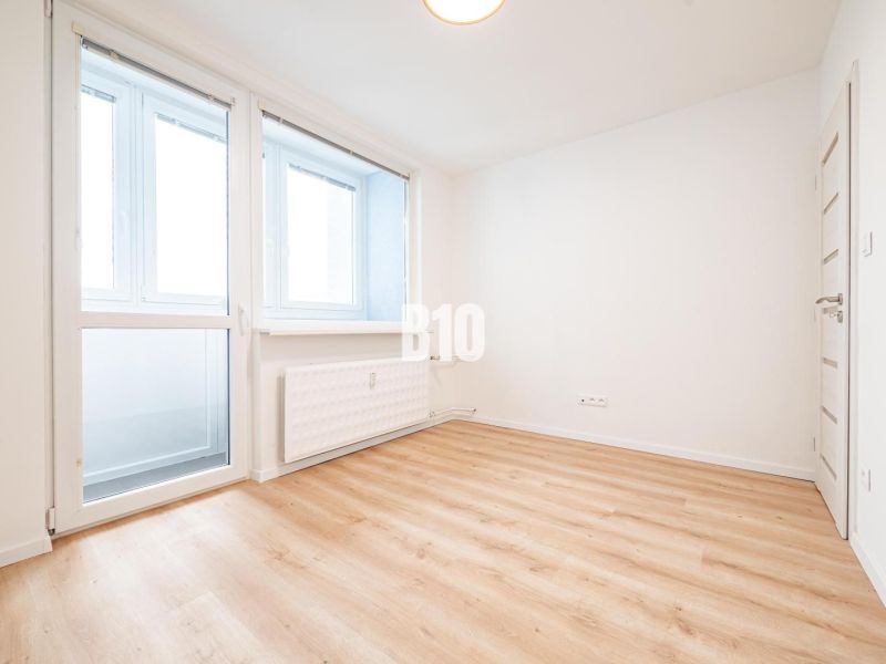 Ein geräumiges Zimmer in einer 3-Zimmer-Wohnung mit großen Fenstern und einem Boden in Holzoptik.