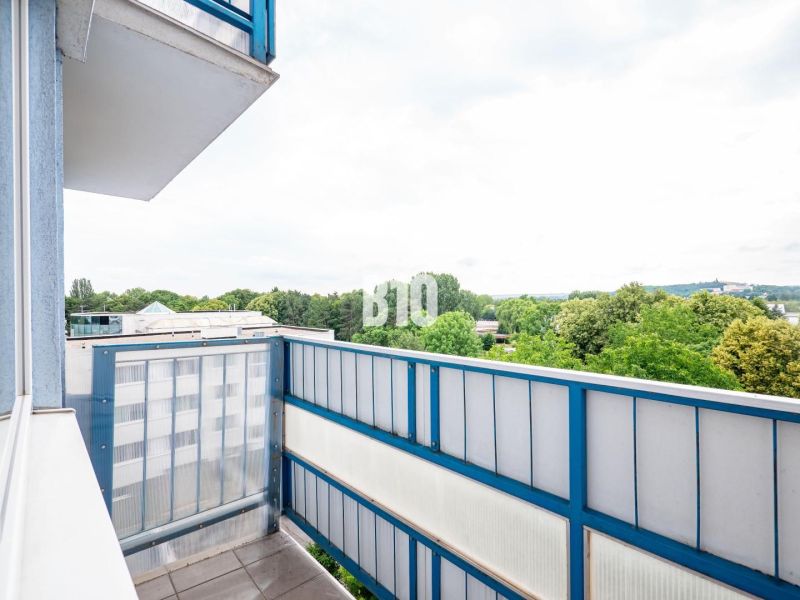 Der Balkon einer 3-Zimmer-Wohnung in Nitra mit Blick auf Grünflächen und Dächer von Gebäuden.