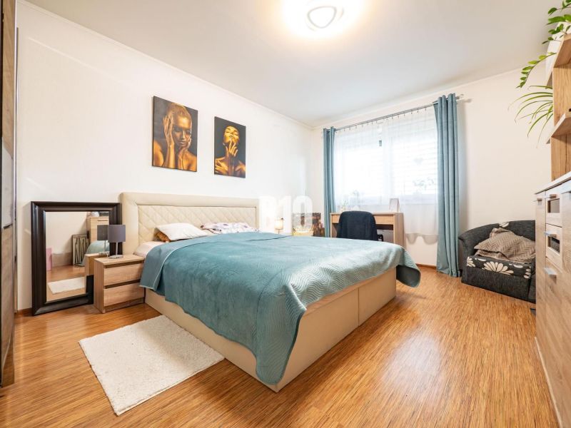 Schlafzimmer im Einfamilienhaus mit Bett, Spiegel und Boden in Holzoptik.