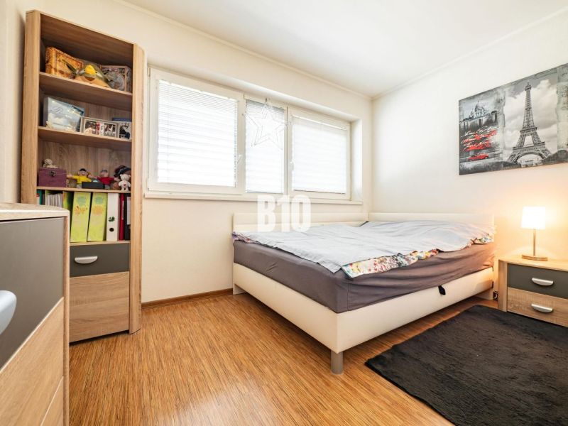 Ein Schlafzimmer in einem Einfamilienhaus mit einem Boden in Holzoptik und einem Regal voller Bücher und Spielzeug.