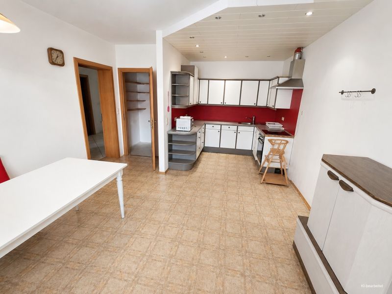 Eine Küche in einem Einfamilienhaus mit roten Akzenten und einem Boden in Holzoptik.