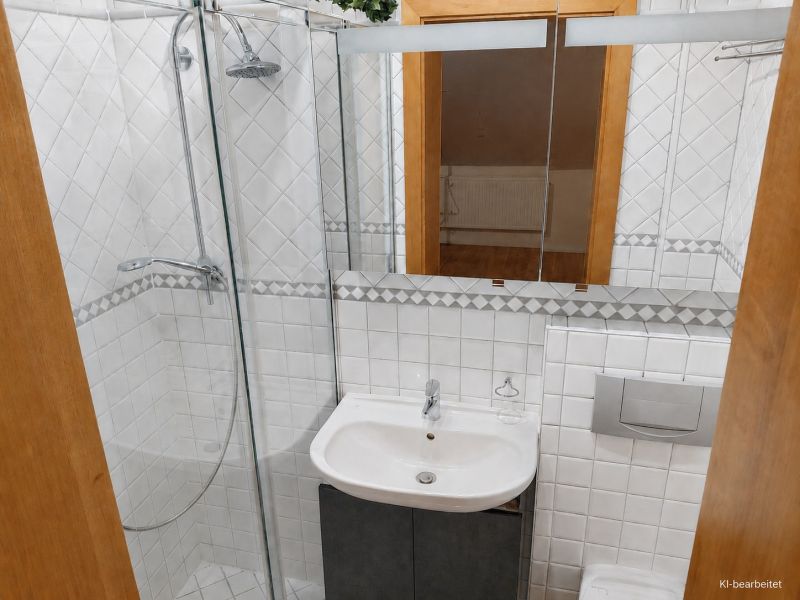 Ein Badezimmer in einem Einfamilienhaus mit weißen Fliesen und einer Duschkabine.