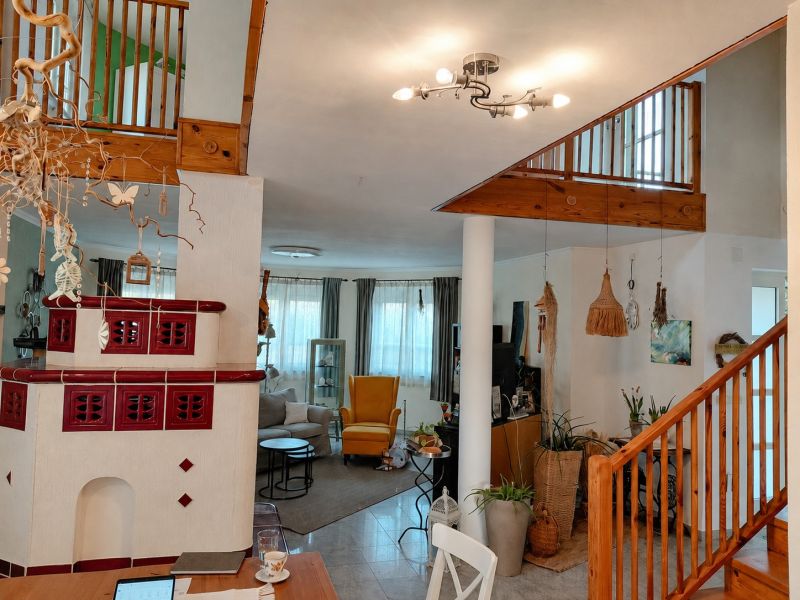 Innenraum eines Einfamilienhauses mit einem Keramikkamin, Pflanzen und einer Holztreppe.