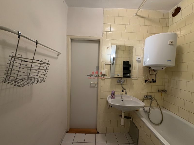 Badezimmer in einer 3-Zimmer-Wohnung mit Waschbecken, Badewanne und Wassererhitzer an der Wand.