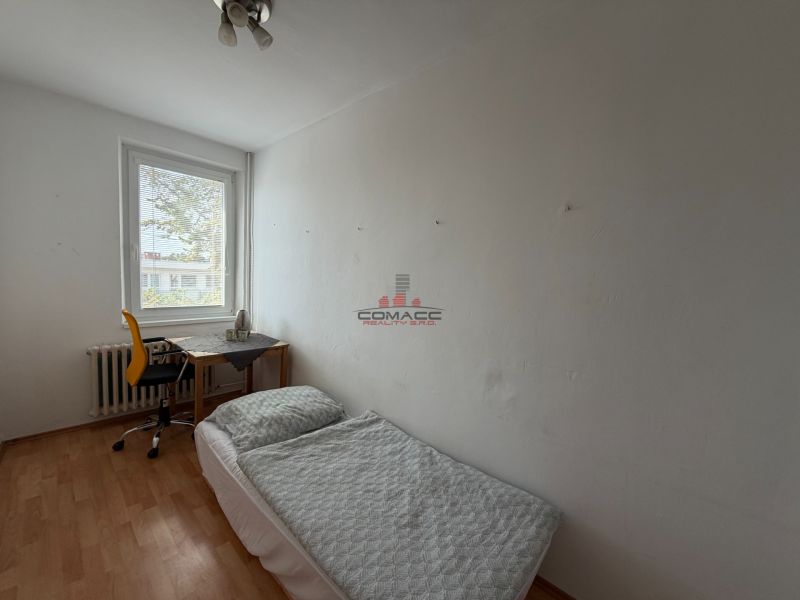 Ein Zimmer in einer 3-Zimmer-Wohnung mit einem Bett, einem Tisch und einem Boden in Holzoptik.